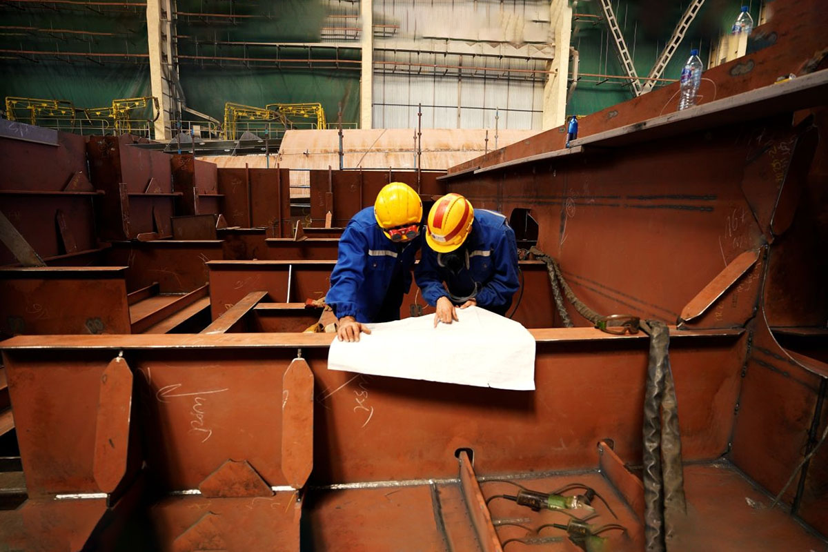 Two fitters are studying technical drawnings of the ship section