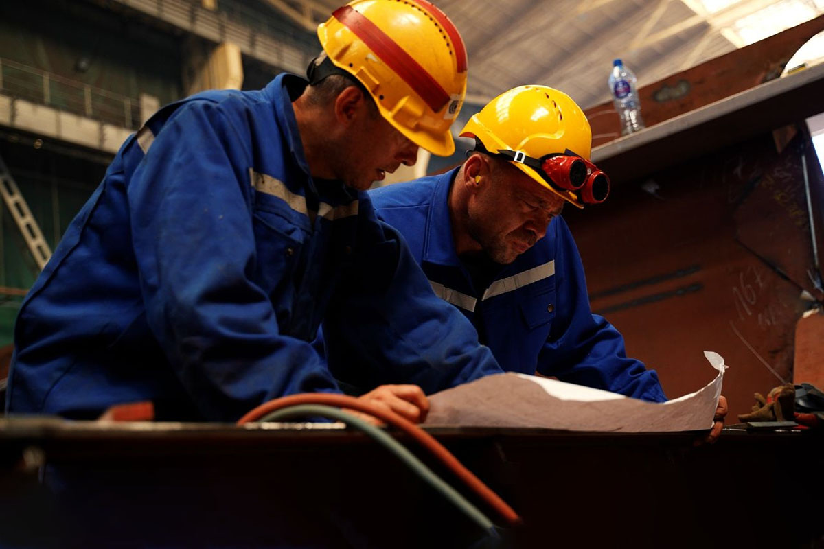 Two fitters are studying technical drawnings of the ship section